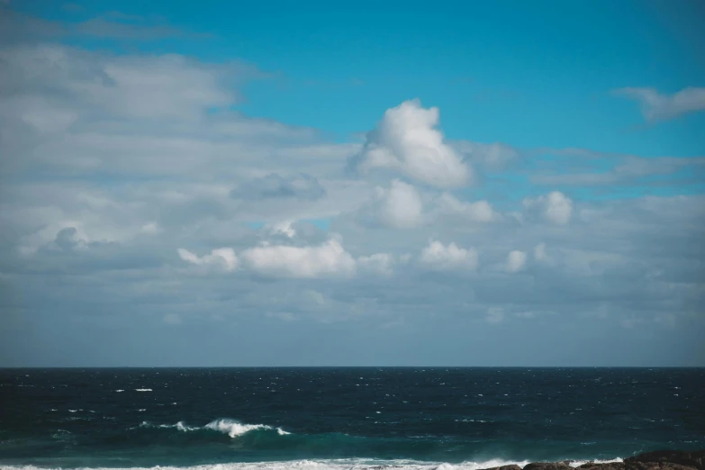 a man flying a kite on top of a sandy beach, unsplash, minimalism, clouds and waves, azores, cumulus clouds, blue