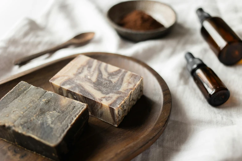 a couple of soap bars sitting on top of a wooden plate, by Emma Andijewska, chocolate. rugged, coffee, lots of swirling, ingredients on the table