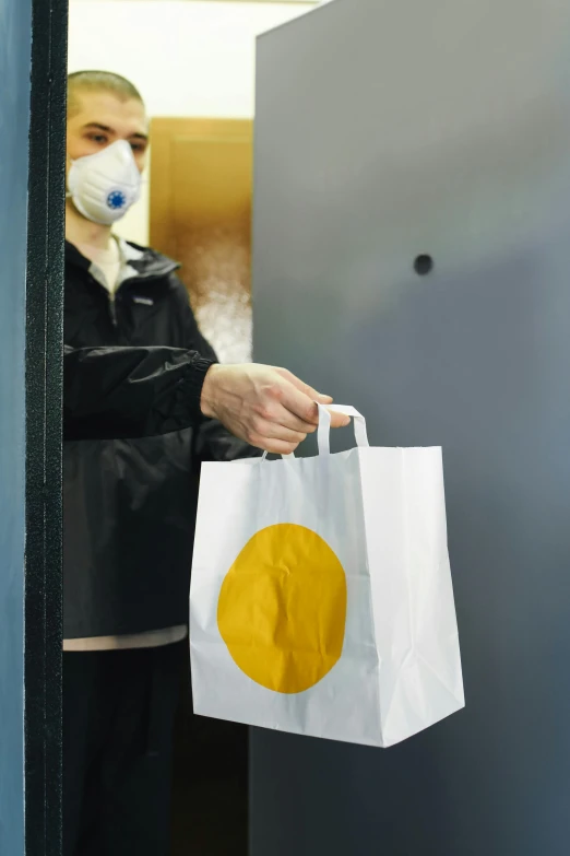 a woman wearing a face mask holding a shopping bag, by Dan Content, private press, opening door, yellow aureole, ecommerce photograph, enso