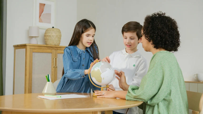 a group of children sitting around a table looking at a globe, by Emma Andijewska, pexels contest winner, sea - green and white clothes, avatar image, tabletop model, decoration