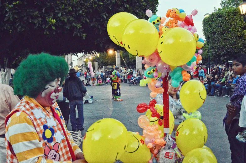 a clown standing next to a bunch of balloons, talaat harb square cairo, instagram picture, witchlight carnival, green and yellow colors