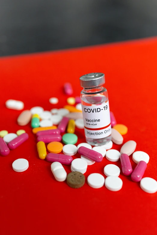 a bottle filled with pills sitting on top of a red table, coronavirus, slide show, daniel richter, multi - coloured