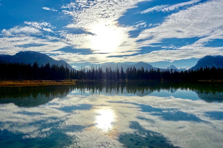 a body of water with trees and mountains in the background, pexels contest winner, land art, banff national park, prismatic cumulus clouds, instagram post, perfect crisp sunlight