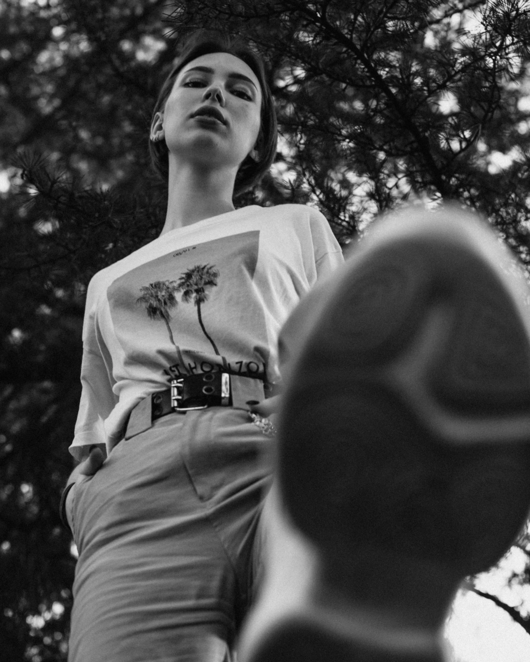 a black and white photo of a woman standing in front of a tree, by Tamas Galambos, unsplash contest winner, hyperrealism, wearing pants and a t-shirt, detailed shot legs-up, as fashion editorial 90s, graphic tees