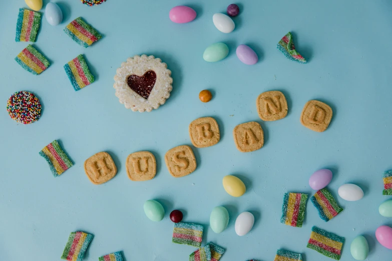 a number of cookies and candies on a blue surface, by Sylvia Wishart, trending on pexels, letterism, handsome man, pride month, shot on hasselblad, on grey background