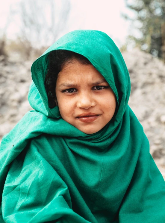 a young girl sitting on top of a pile of rocks, by Riza Abbasi, pexels contest winner, hurufiyya, with a green cloak, closeup of face, close-up portrait film still, covered with blanket