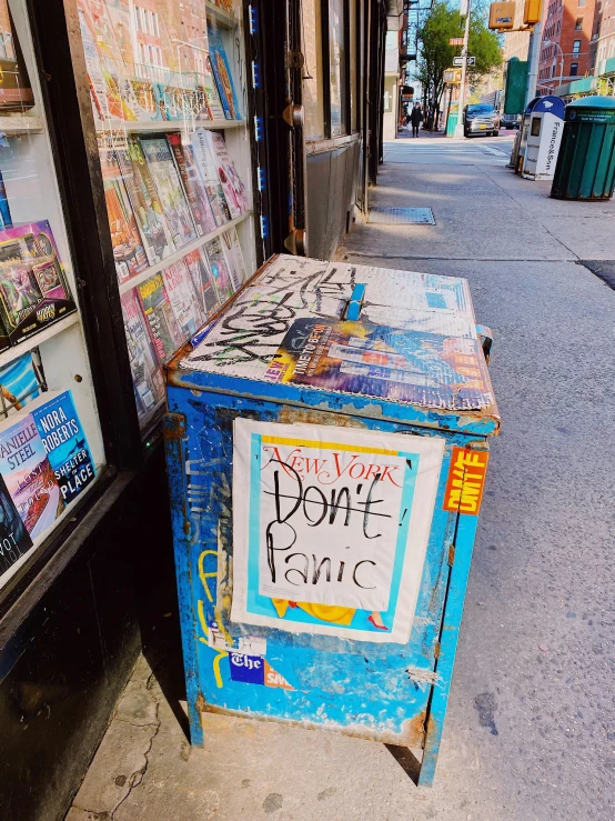 a newspaper box sitting on the side of a street, an album cover, by Bernie D’Andrea, trending on pexels, graffiti, sonic youth, post apocalyptic new york, blue paint on top, panic