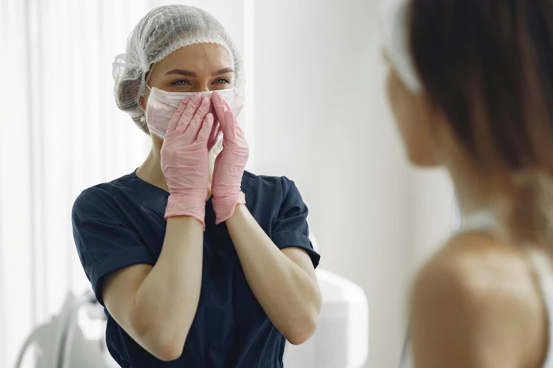 a woman wiping her face in front of a mirror, a picture, shutterstock, hurufiyya, masked doctors, flirting, surgical gown and scrubs on, large noses