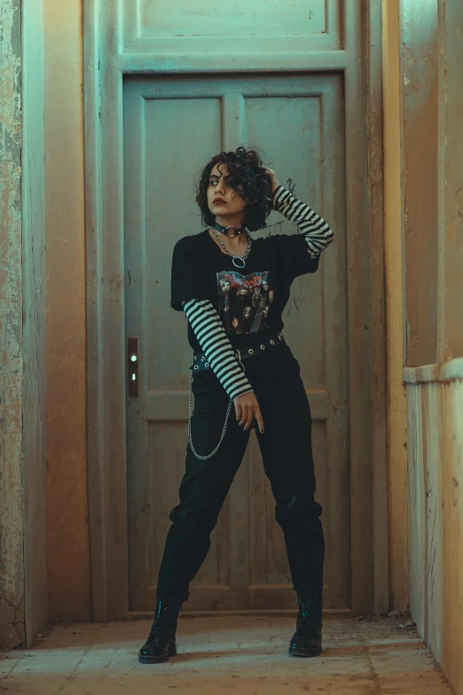 a woman standing in a hallway next to a door, an album cover, inspired by Elsa Bleda, pexels contest winner, wearing a punk outfit, (dark shorter curly hair), doing a sassy pose, streetwear