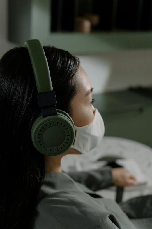 a woman sitting on a bed wearing headphones, trending on pexels, hyperrealism, green facemask, on a advanced lab, over the shoulder closeup, made of high tech materials