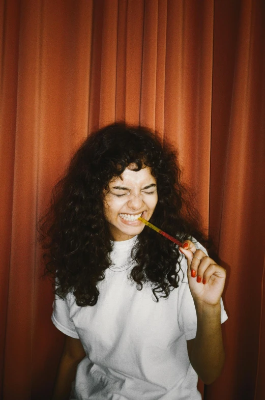 a woman brushing her teeth in front of a red curtain, by Nathalie Rattner, long black curly hair, holding hot sauce, gummy bear, trending on vsco