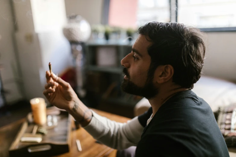 a man sitting at a desk in front of a computer, a portrait, by Jessie Algie, pexels contest winner, smoking a bowl of hash together, a portrait of rahul kohli, looking at his phone, at a dinner table