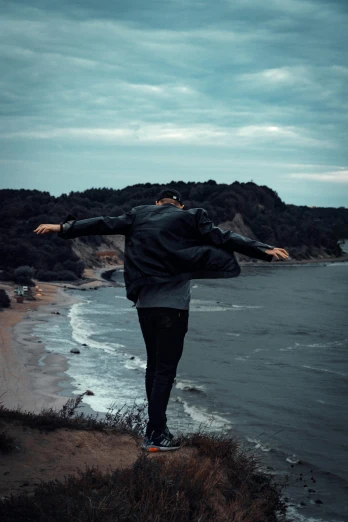 a man standing on top of a cliff next to the ocean, pexels contest winner, romanticism, dynamic dancing pose, half turned around, slight overcast, he is dancing