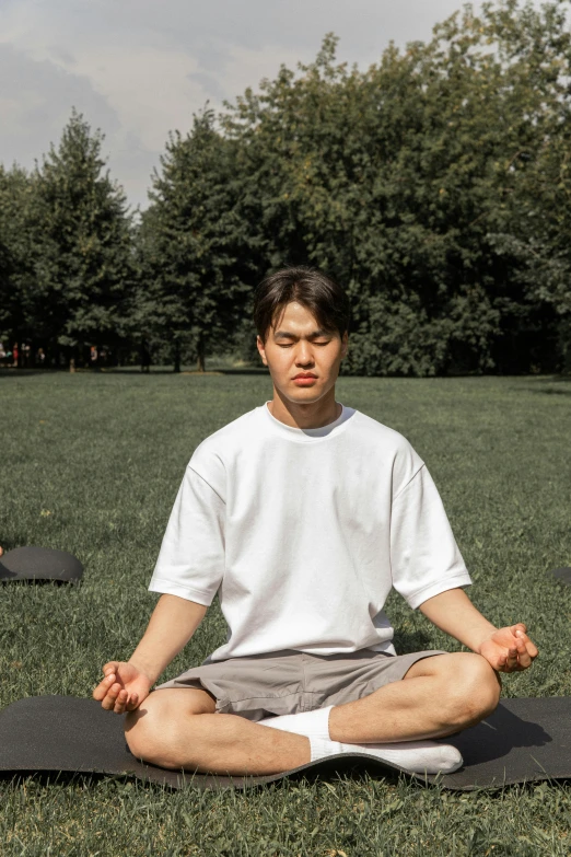 a man sitting on a yoga mat in a park, by Kim Tschang Yeul, unsplash, renaissance, centered in portrait, low quality photo, wearing a tee shirt and combats, good posture