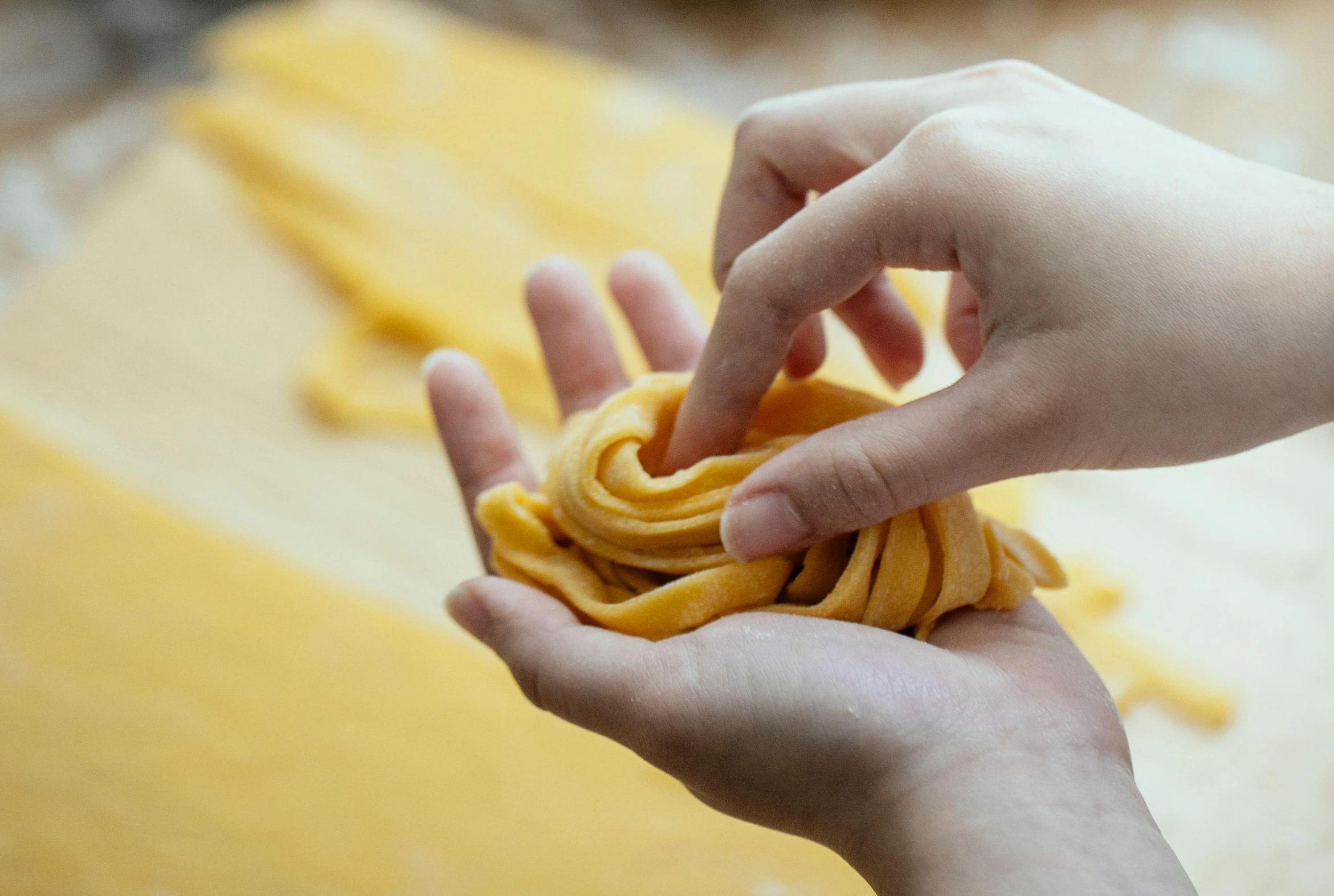 a person holding a piece of pasta in their hand, process art, with yellow cloths, spiralling, easy to use, up close