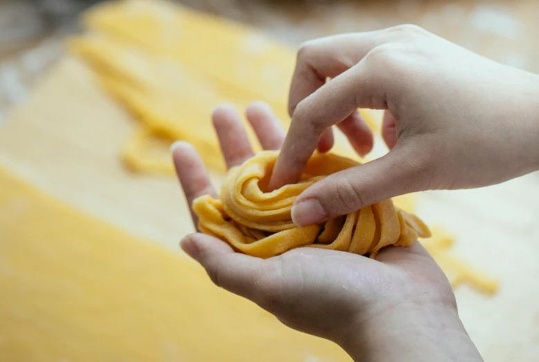 a person holding a piece of pasta in their hand, process art, with yellow cloths, spiralling, easy to use, up close