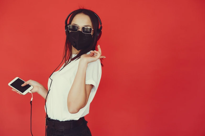 a woman wearing headphones and holding a cell phone, an album cover, trending on pexels, aestheticism, black mask, black red white clothes, red wall, outfit photo