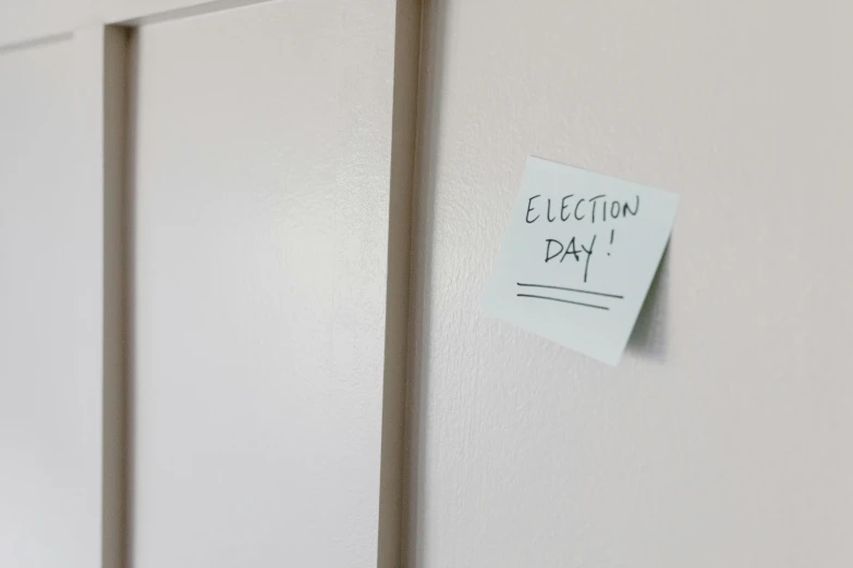 a note pinned to a wall with the word election day written on it, pexels, temporary art, hung above the door, me
