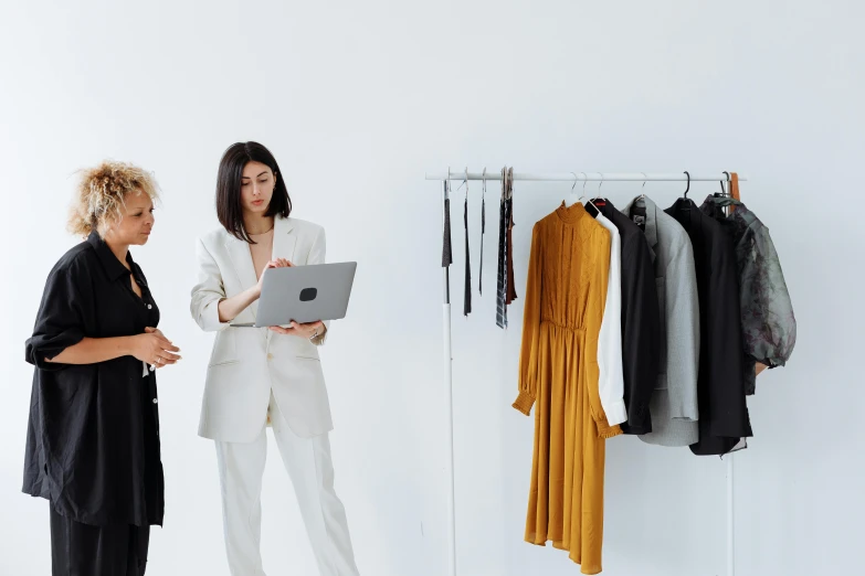 two women standing next to each other looking at a laptop, by Carey Morris, pexels contest winner, renaissance, business clothes, presenting wares, minimalistic, elaborate clothing