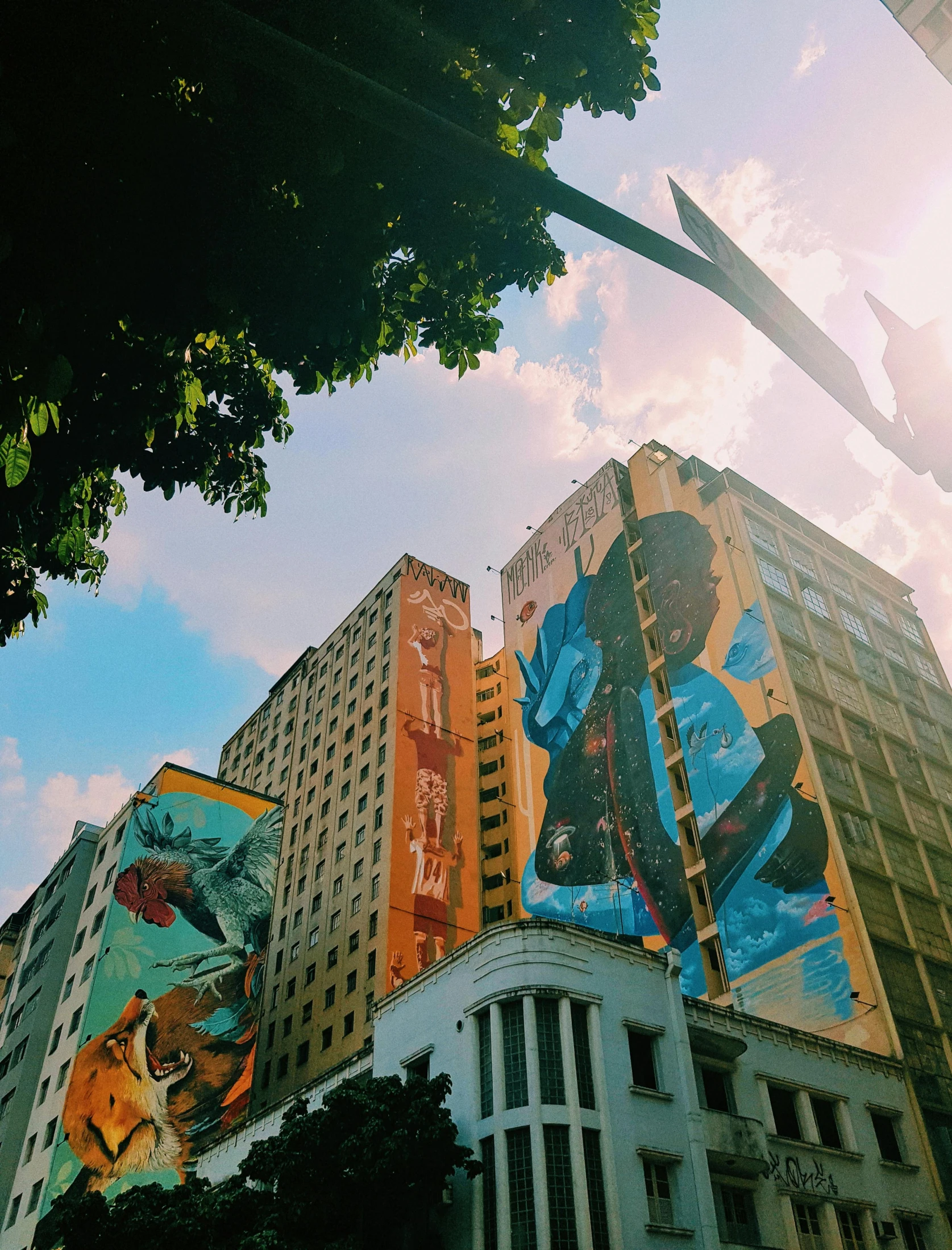 a tall building with a mural on the side of it, a photo, pexels contest winner, sao paulo in the year 2 0 7 0, mucha vibe, low angle photo, 🪔 🎨;🌞🌄