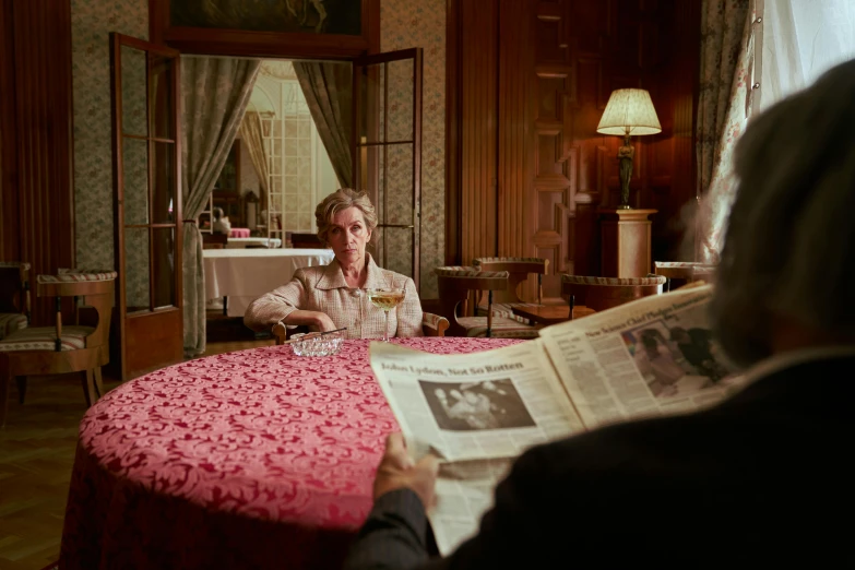 a woman sitting at a table reading a newspaper, by Wes Anderson, vesper lynd from casino royale, cinematic photograph, image