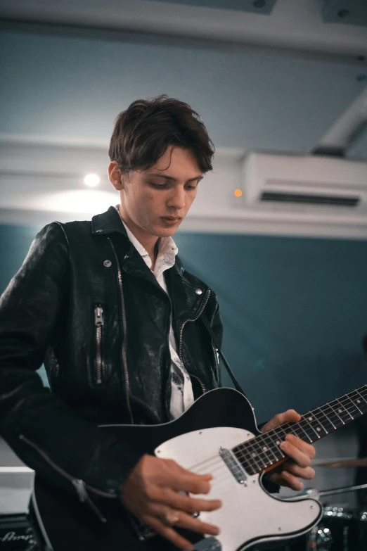 a man in a leather jacket playing a guitar, trending on unsplash, bauhaus, androgynous face, meredit frampton style, with high cheekbones, live performance