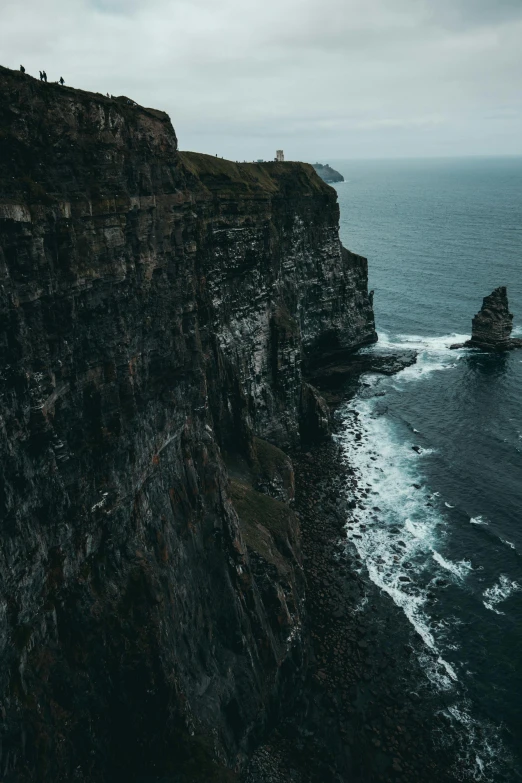 a person standing on top of a cliff next to the ocean, by Eamon Everall, pexels contest winner, ireland, flying over the ocean, low quality photo, telephoto shot