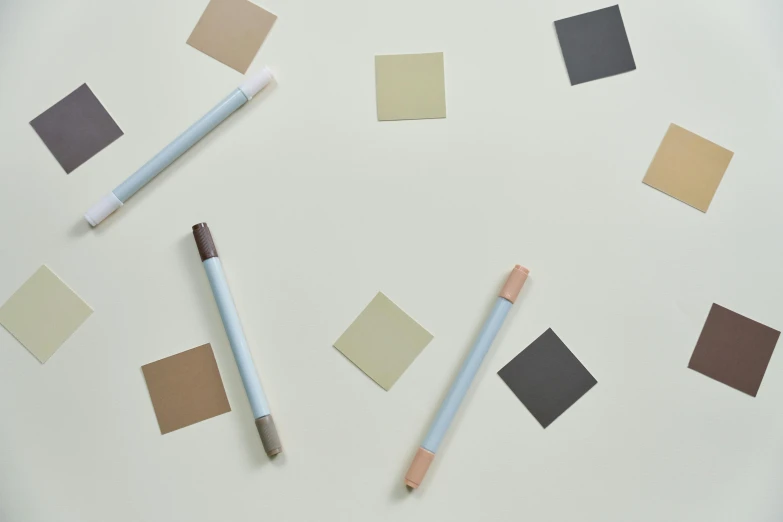 a group of pencils sitting on top of a white table, an abstract drawing, inspired by Agnes Martin, color field, taupe, light grey blue and golden, 3 colours, squares