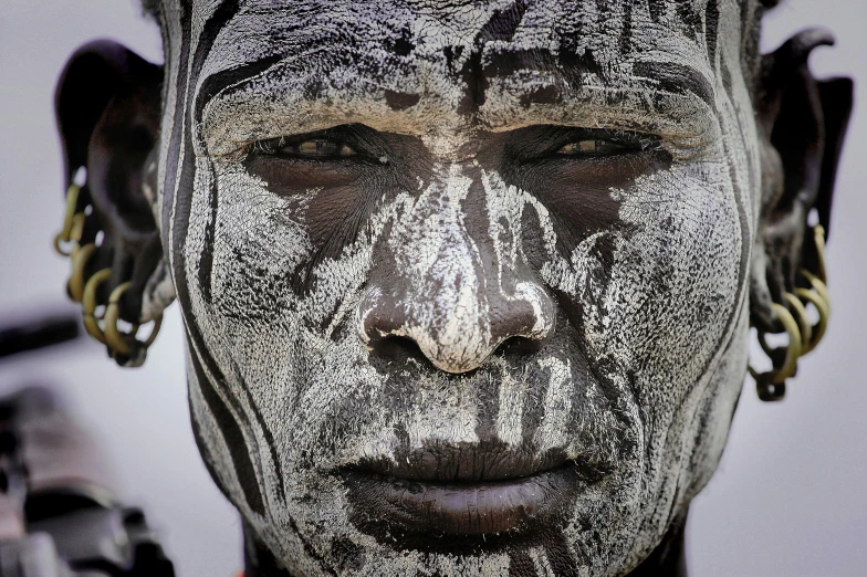 a close up of a person with white paint on their face, inspired by Albert Namatjira, pexels contest winner, wearing tribal armor, gray anthropomorphic, image credit nat geo, ancient”