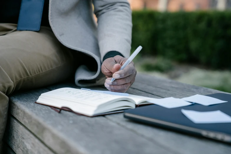 a person sitting on a bench writing on a notebook, happening, sleek hands, holding books, malcolm hart, at college