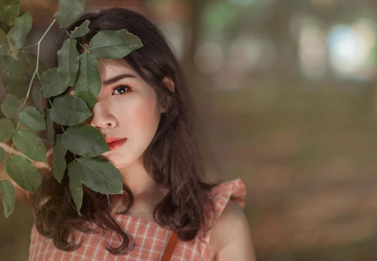 a woman holding a leaf in front of her face, a picture, trending on pexels, aestheticism, coral brown hair, oriental face, with soft bushes, portrait”