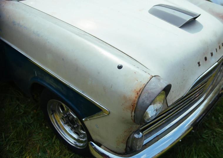 a white and blue car sitting on top of a lush green field, unsplash, photorealism, metal skin with some scratches, restoration, pointed face, flat shaped chrome relief