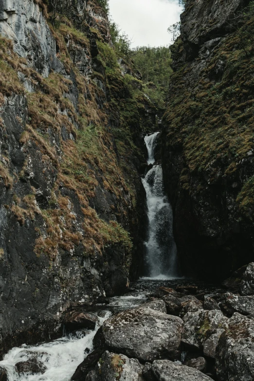 a man standing in front of a waterfall, by Daniel Seghers, pexels contest winner, hurufiyya, in scotland, high angle close up shot, in between a gorge, small creek