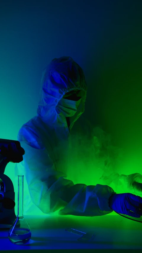 a person sitting at a table in front of a green light, a microscopic photo, pexels, holography, staff wearing hazmat suits, rgb lighting, cold blue light, wearing a labcoat