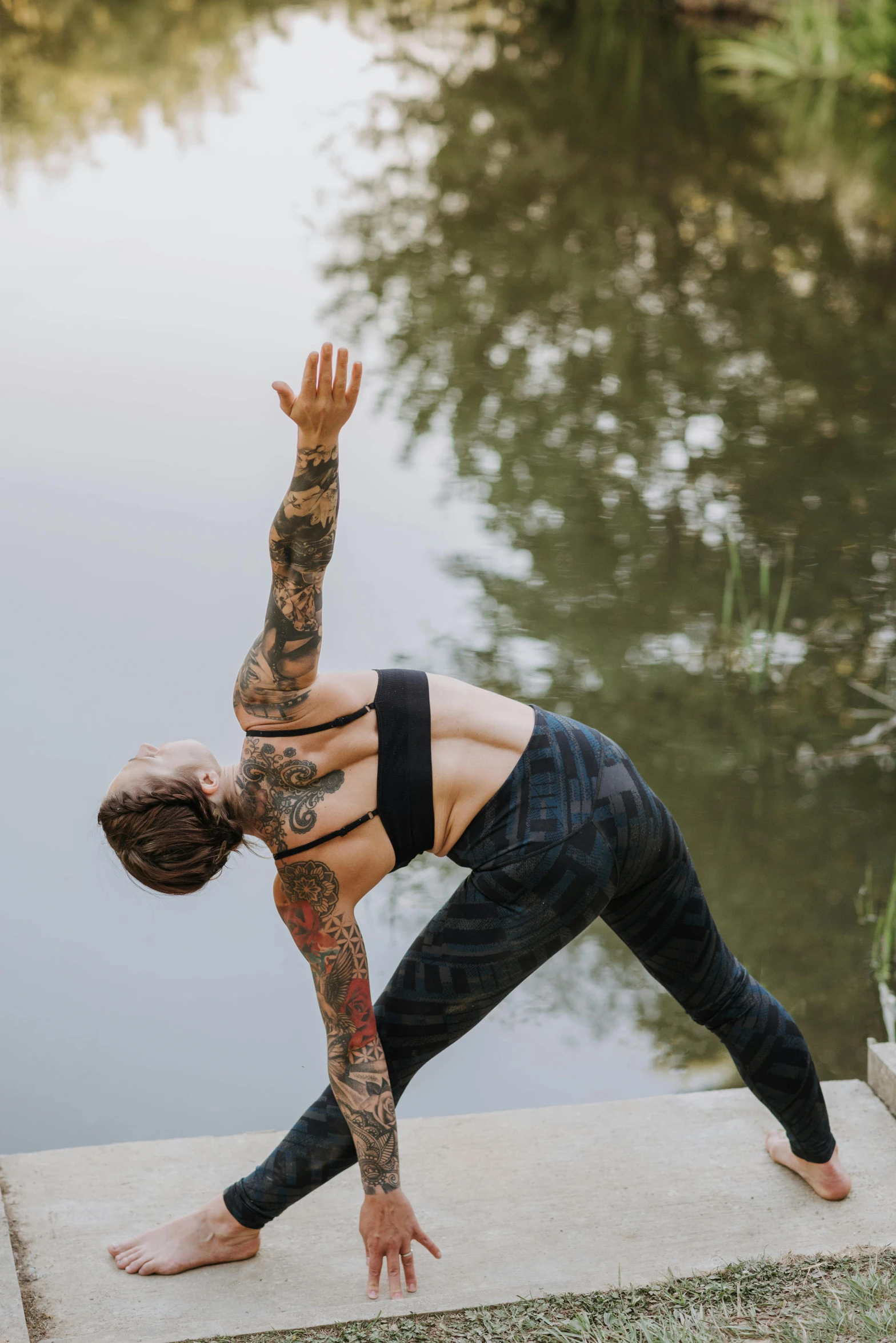 a woman doing a yoga pose in front of a body of water, a tattoo, botanicals, triangle, action sports, connectivity