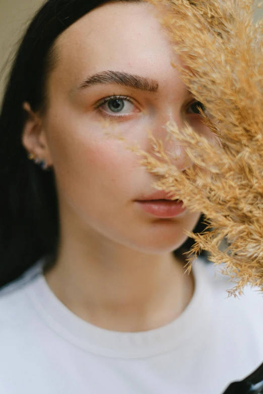 a woman holding a dried plant in front of her face, trending on pexels, beauty portrait, with soft bushes, half face, portrait sophie mudd