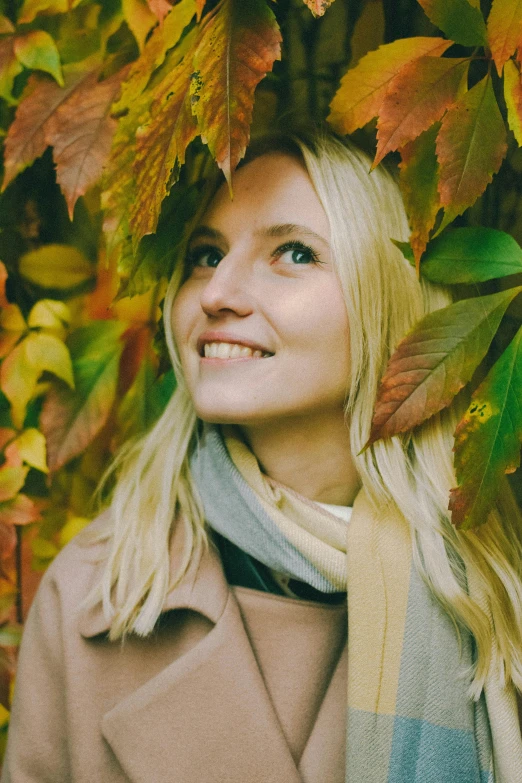 a woman standing in front of a bunch of leaves, by Grytė Pintukaitė, pexels contest winner, 2 5 6 x 2 5 6 pixels, blonde swedish woman, turning her head and smiling, detailed color scan