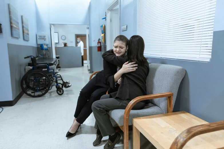 a couple of women sitting on top of a couch, hospital room, hugging her knees, jordan grimmer and natasha tan, production still