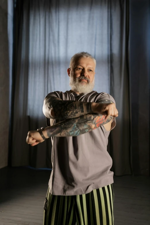a man standing in front of a window holding a baseball bat, a tattoo, inspired by Lajos Vajda, silver hair and beard, insectile forearms folded, colour photograph, against dark background
