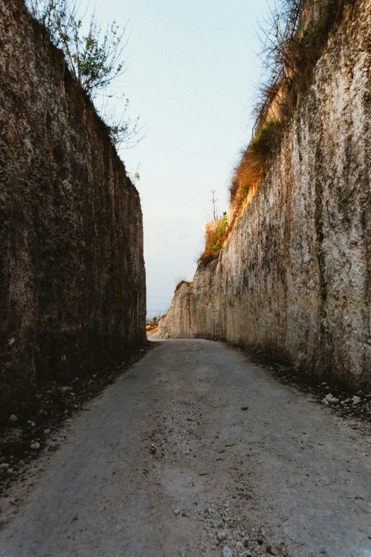 a man riding a skateboard down a dirt road, an album cover, inspired by Alberto Burri, unsplash, renaissance, rock walls, indonesia, wide view, late morning