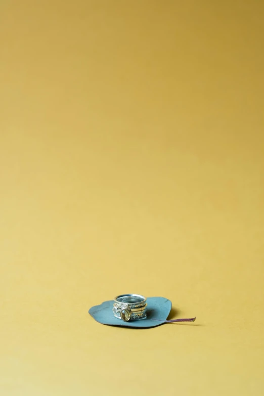 a cup sitting on top of a blue plate, an album cover, by Alison Geissler, minimalism, ten-gallon hat, jewelry, 9 0 mm studio photograph tiny, on yellow paper