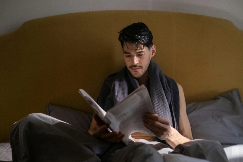 a man sitting on a bed reading a book, f 1 driver charles leclerc, covered with blanket, ignant, profile image