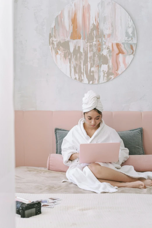 a woman sitting on a bed using a laptop, trending on pexels, happening, pastel pink robes, skincare, post graduate, wearing a towel