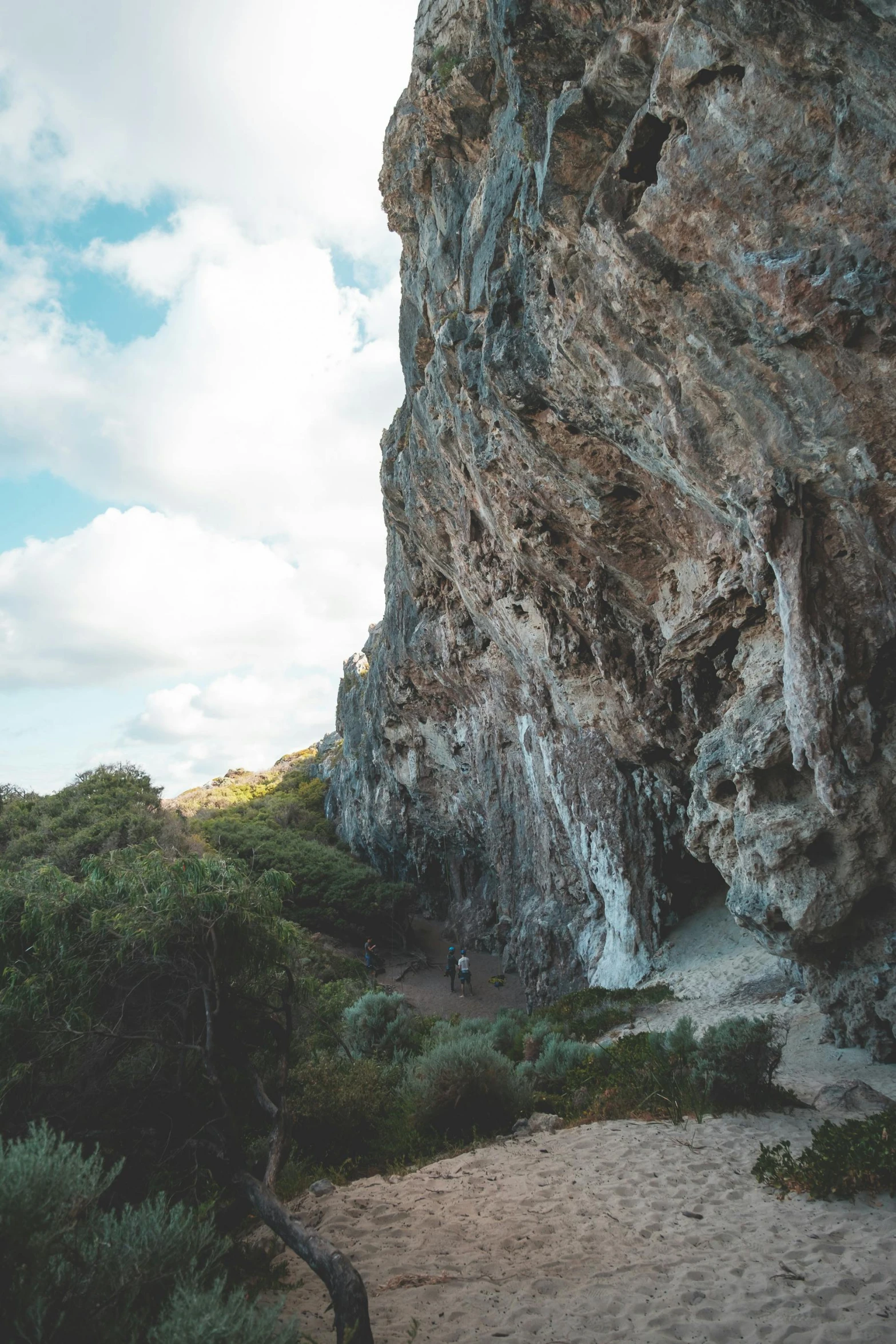 a man standing on top of a sandy beach next to a cliff, speleothems, marbella landscape, sydney park, rock climbers climbing a rock