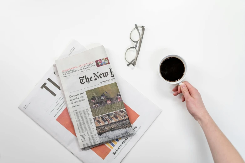 a person holding a cup of coffee next to a newspaper, a picture, detailed product image, new york times, on grey background, set against a white background