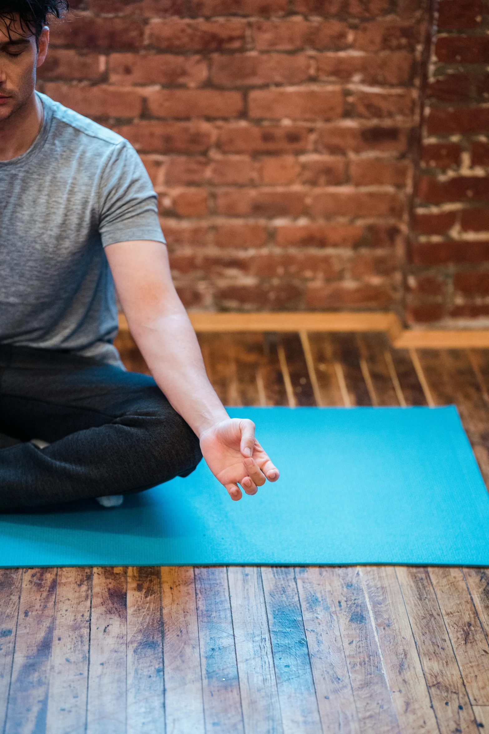 a man sitting on a yoga mat in front of a brick wall, by Dan Content, unsplash, square, panoramic shot, insectile forearms folded, indoor picture