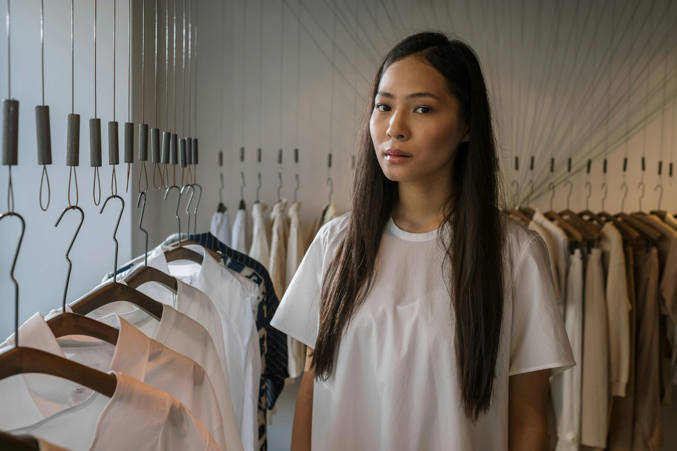 a woman standing in front of a rack of clothes, inspired by Kim Tschang Yeul, happening, wearing white shirt, looking towards camera, darren quach, uncropped