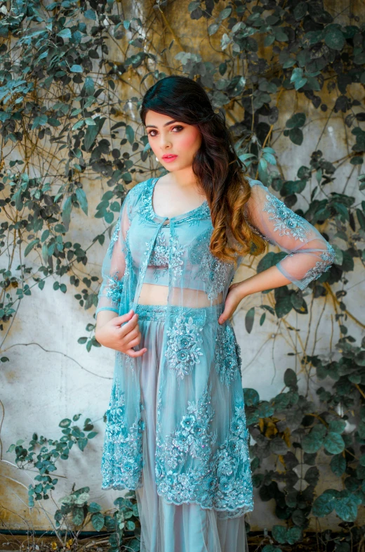 a woman in a blue dress standing in front of a wall, an album cover, by Robbie Trevino, renaissance, intricate and detailed lace set, with teal clothes, south east asian with long, pr shoot