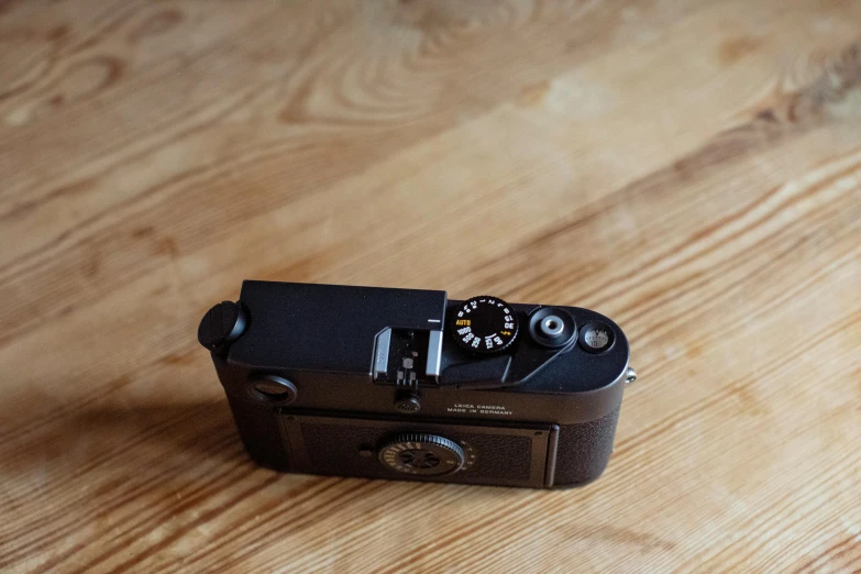 a camera sitting on top of a wooden table, by Niels Lergaard, unsplash, private press, leica m6, black matte finish, turned back to camera, a high angle shot