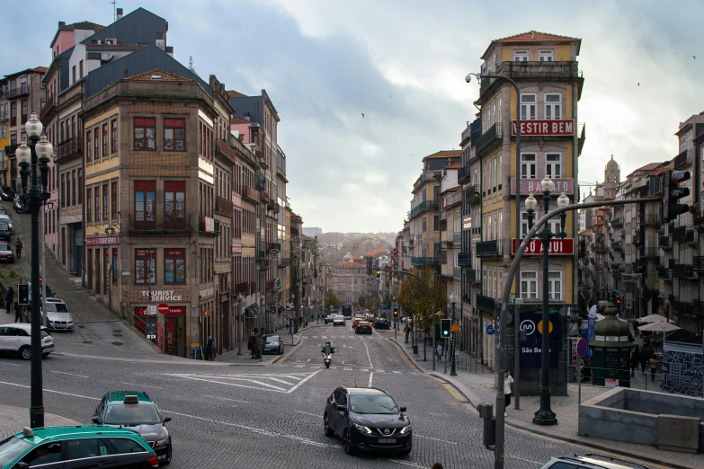 a group of cars driving down a street next to tall buildings, a photo, inspired by Almada Negreiros, pexels contest winner, renaissance, baroque winding cobbled streets, city on a hillside, grey, square
